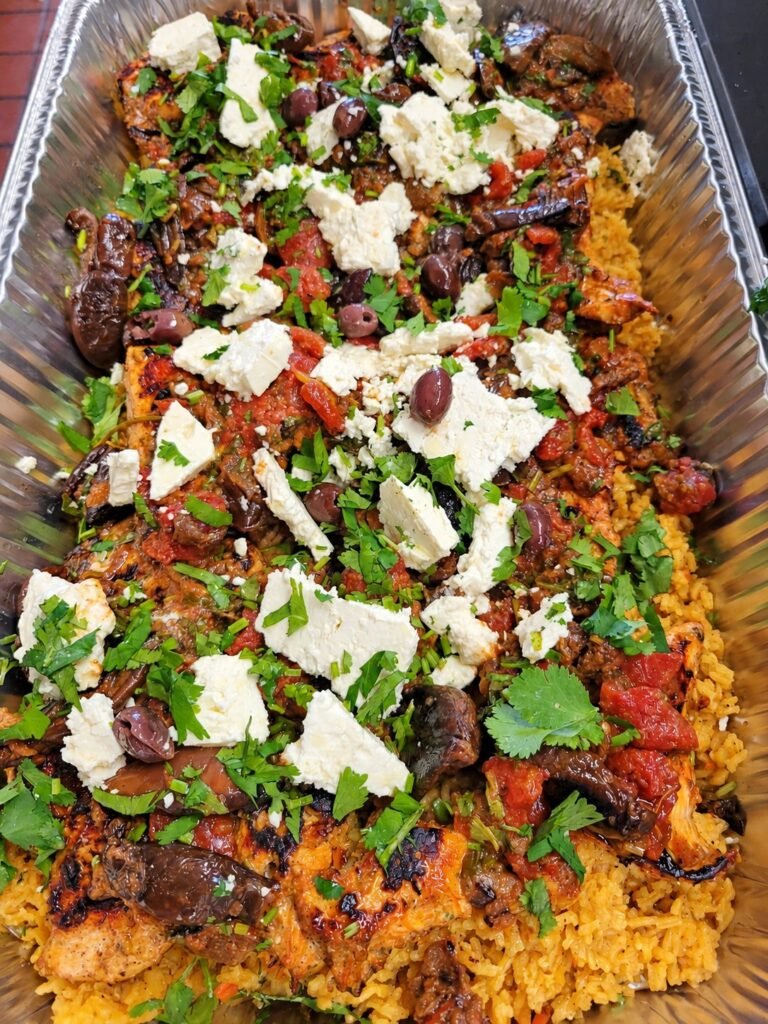 Catered rice dish topped with meat, olives, cheese and herbs